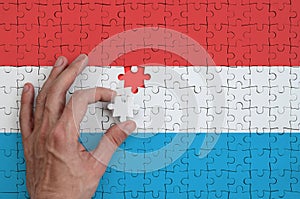 Luxembourg flag is depicted on a puzzle, which the man`s hand completes to fold