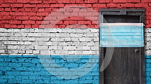 Luxembourg flag painted on brick wall and closed door with medical mask protected