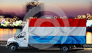 Luxembourg flag on the side of a white van against the backdrop of a blurred city and river. Logistics concept