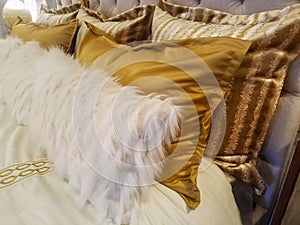 Luxiourous gold and fur pillow shams on bed propped against quilted beadstead