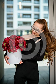 Luxirious bouquet of dark red peonies in white hat box in woman& x27;s hands photo