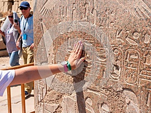 Luxor, Egypt - October 3, 2021: Woman touches her hand to a wall with ancient Egyptian hieroglyphs and drawings of a statue of a