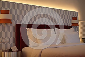 Luxurious bed from a hotel room suite with red, orange and grey tones along with four pillows