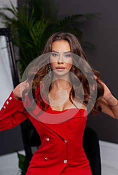 Luxurious brunette with bright makeup posing in red dress in interior and demonstrate her chestnut curly hair