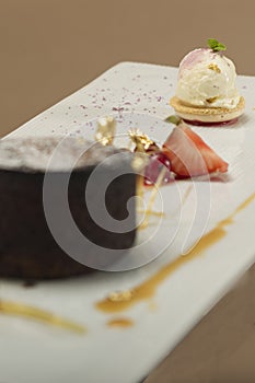 Luxurious dessert with brownie,  vanilla ice-cream placed on a macaron,  strawberries,  mint,  decorated with gold leafs and