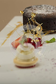 Luxurious dessert with brownie,  vanilla ice-cream placed on a macaron,  strawberries,  mint,  decorated with gold leafs and