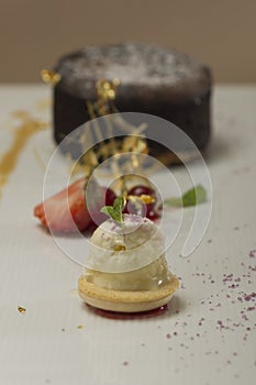 Luxurious dessert with brownie,  vanilla ice-cream placed on a macaron,  strawberries,  mint,  decorated with gold leafs and