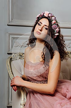 Luxurious girl in an evening cloudy dress sitting on a sofa in the studio interior.