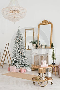 The luxurious interior of the living room with a fireplace and a Christmas tree, gifts and a stepladder. Classic interior in white