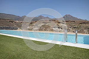 Luxurious long swimming pool overlooking the arid volcanic mountains, surrounded by a perfectly trimmed lawn