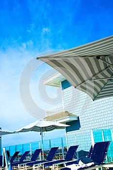 A luxurious resort provides rows of umbrellas and chairs for pampered guests to recline and relax under a deep blue sky