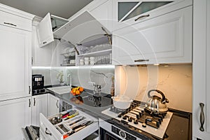 Luxurious white modern kitchen interior, drawers pulled out, doors open
