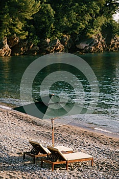 Luxurious wooden sun loungers and green beach umbrellas, on a sandy beach in Milocer Park, near Sveti Stefan Island