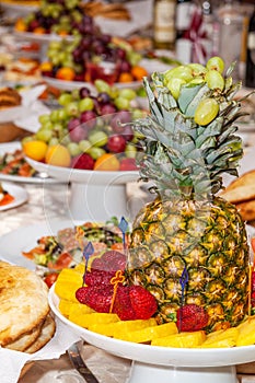 Luxuriously decorated table with tropical fruits, strawberries, bread and pineapple