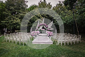 A luxury alfresco wedding ceremony set up at the countryside; white rustic tiffany chairs, flower arrangements along the aisle