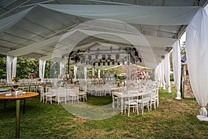 A luxury alfresco wedding reception set up at the countryside; white rustic tiffany chairs, top table flower arrangements and