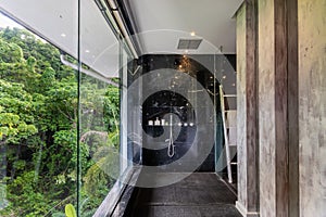 Luxury bathroom black with marble wall has a large glass window overlooking the trees and nature