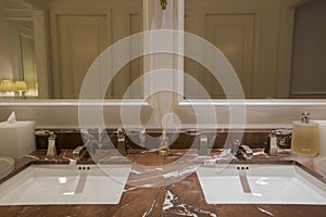 Luxury bathroom with brown beige granite marble stone counter vanity top board, two white ceramic sinks, large rectangular mirrors