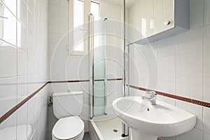 Luxury bathroom is lined with white ceramic tiles with shower toilet and sink with a narrow vertical windows for natural