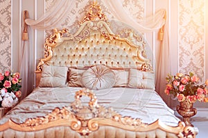 Luxury bedroom in light colors with golden furniture details. Big comfortable double royal bed in elegant classic