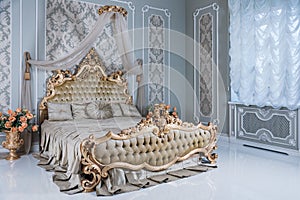 Luxury bedroom in light colors with golden furniture details. Big comfortable double royal bed in elegant classic