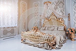 Luxury bedroom in light colors with golden furniture details. Big comfortable double royal bed in elegant classic