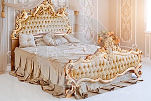 Luxury bedroom in light colors with golden furniture details. Big comfortable double royal bed in elegant classic