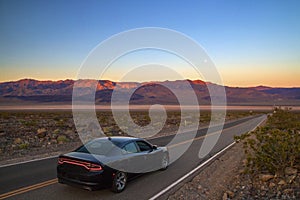 Luxury black fast American car driving on desert highway in Death Valley California, road trip, colourful sunrise mountains view