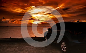 Luxury blue SUV car parked on concrete road by the sea at sunset with dramatic sky and clouds. Electric car technology and busines