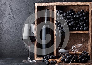 Luxury bottle of red wine with dark grapes inside vintage wooden box on black stone background. Elegant wine glass with corks and