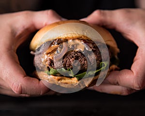 Luxury burger with a brioche bun on black background. Hands grabbing burger