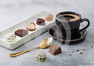 Luxury Chocolate candies in white porcelain plate with cup of black coffee and golden spoon on light table background