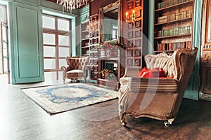 Luxury classic interior of home library. Sitting room with bookshelf, books, arm chair, sofa and fireplace