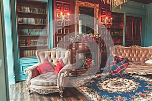 Luxury classic interior of home library. Sitting room with bookshelf, books, arm chair, sofa and fireplace