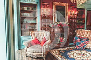 Luxury classic interior of home library. Sitting room with bookshelf, books, arm chair, sofa and fireplace