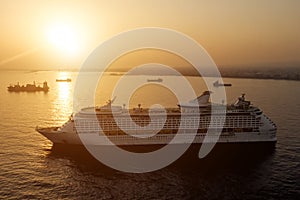 The luxury cruise liner in a port near big sea city during sunset.