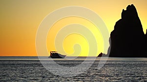 Luxury cruise trip. Red burning sunset over the sea with silhouette of rich yacht and rocky volcanic cliff. Abstract