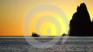 Luxury cruise trip. Red burning sunset over the sea with silhouette of rich yacht and rocky volcanic cliff. Abstract
