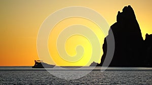 Luxury cruise trip. Red burning sunset over the sea with silhouette of rich yacht and rocky volcanic cliff. Abstract