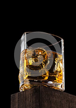 Luxury crystal glass with ice cubes of scotch whiskey on top of wooden box and black