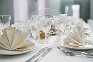 Luxury dinner set arranged on a table with vintage cream lace tablecloth and napkins, elegant porcelain dishes, silverware and