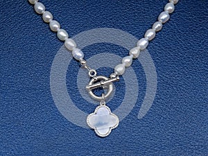 Luxury elegant baroque pearl necklace with pendant on dark blue textured leather background