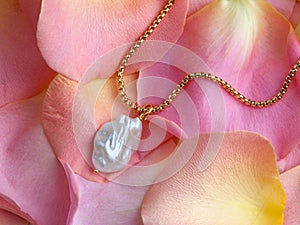 Luxury elegant baroque pearl pendant with golden chain on pink yellow rose petals