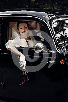 luxury elegant wedding couple kissing in stylish black car. gorgeous bride and handsome groom in retro style. romantic moment