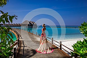 Luxury fashion. Elegant fashion model is posing outdoor. Stylish female model in long gown dress on the Maldives beach. Elegance.