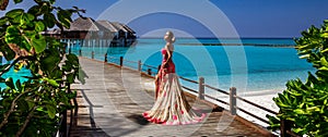 Luxury fashion. Elegant fashion model is posing outdoor. Stylish female model in long gown dress on the Maldives beach. Elegance.