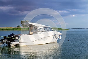 Luxury fishing motor boat moored at coast in bay on river or lake. Dark stormy sky with thunder clouds on background. Travel and r