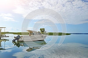 Luxury fishing motor boat moored at coast in bay on river or lake. Scenic blue sky with fluffy white clouds on