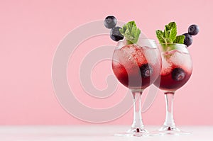 Luxury fresh cold red summer fruit cocktails with ice cubes, blueberry, green mint in elegant modern pink kitchen interior.