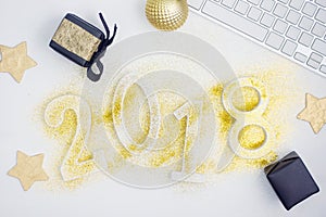 Luxury glowing numbers 2018 made from gold shiny glitter on white table with keyboard and christmas decoration.